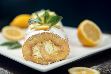 Lemon roll cake decorated with slices of lemon fruit and leaves of min