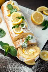 Lemon roll cake decorated with slices of lemon fruit and leaves of mint