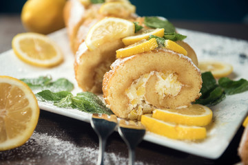 Lemon roll cake decorated with slices of lemon fruit and leaves of mint