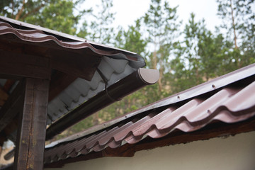 part of a brown gutter with a metal and plastic pipe hangs under the roof of a house on the street