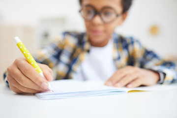 Close up of cute African boy writing in notebook while doing homework, focus on foreground, copy...