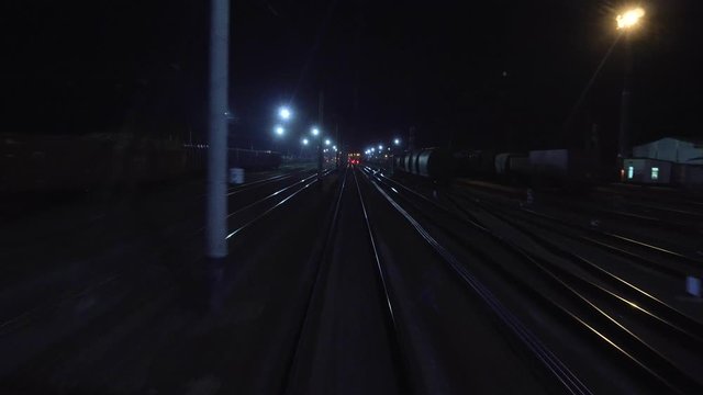 Railroad train passes through railway fork at night. View on rails from rear back window of last coach carriage in motion. Travel and tourism concept. Passenger train going outside of town