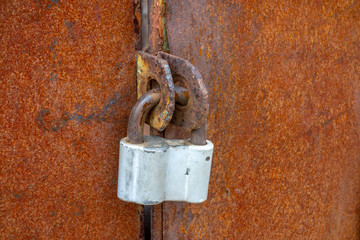 An old padlock hanging on a rusty gate. The entrance is closed.