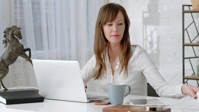 Young business woman working at desk with laptop computer in home office. Slow pan to right.
