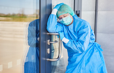 Arzt in Schutzkleidung macht Pause an Tür wegen Stress und Erschöpfung