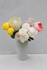 
Bouquet of beautiful bright flowers in a vase on a gray background. Flower concept. Stylish bouquet of peonies, buttercups and protea.
