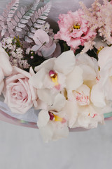 Beautiful bouquet of flowers in the package. Stylish bouquet of flowers in a box. Bouquet of flowers from roses, white orchids, peonies and eustomas. Flower concept.