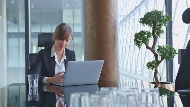 Businesswoman working at desk with laptop computer and smart phone in corporate office, thinking, looking busy. 4K video footage.