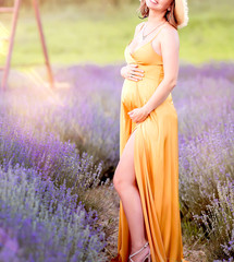 Happy young pregnant woman
in a yellow dress in lavender field. Provence, Lavender, summer. Copy space. Pregnancy and motherhood concept.