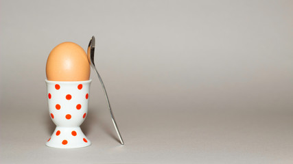 Ein Ei in einem Eierbecher mit einem Löffel angelehnt isoliert vor grauem Hintergrund