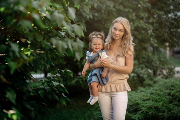 Young blonde mom holds daughter in her arms in summer park