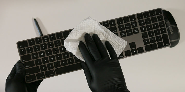 Wearing Gloves To Wipe Down Computer Keyboard And Disinfect The Keys. With Mouse And Tablet Stylus In Background