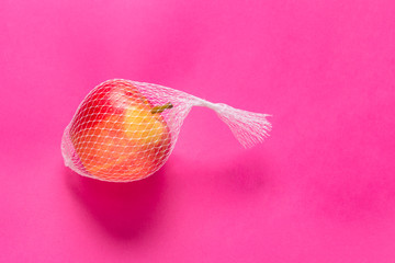 Single red apple in white mesh on blue background