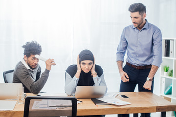 Muslim businesswoman covering ears near multiethnic colleagues in office
