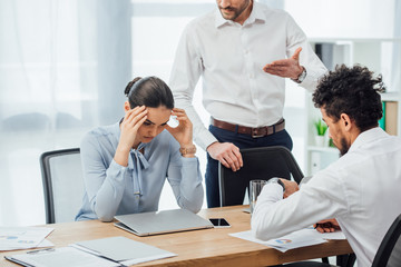 Selective focus of businessman pointing with hand near mexican colleague at table in office