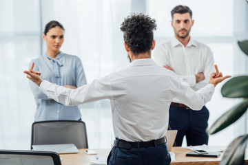 Selective focus of african american businessman showing middle fingers at multiethnic colleagues in...