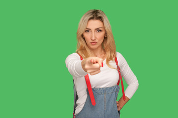 Are you ready? Portrait of serious adult blond woman in stylish denim overalls pointing finger to...
