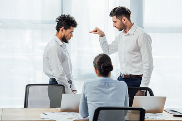 Selective focus of businessman pointing with finger at offended african american colleague in office
