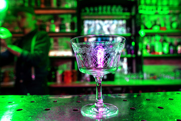 Close up of graceful drinking glass on a bar counter, preparation for a cocktail. Entertainment, tasty and crafted drinks, service concept. Modern bar, trendy neoned colors. Bright, vibrant colors.