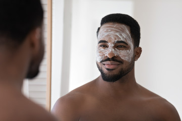 Handsome young african American man look in mirror in bathroom use facial blackhead pore removal...