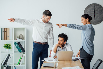 Multiethnic business people pointing with fingers at african american businessman at table in office