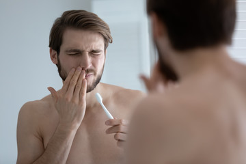 Young caucasian man wash brush teeth in bathroom have painful feeling suffer from gingivitis or...
