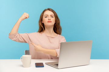 Independent strong confident woman boss sitting at workplace with laptop and showing biceps,...