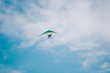 The hang glider flying on background blue sky with clouds.