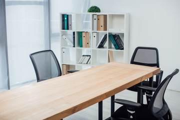 Wooden table and chairs near rack with paper folders in office