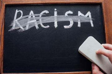 Cropped view of man holding chalkboard cleaner near lettering racism