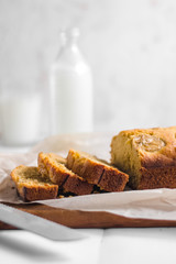 Homemade sliced healthy banana bread ready for serve on breakfast on the white concrete background with craft baking paper and pastry knife, glass of milk. Top view. Close up shoot