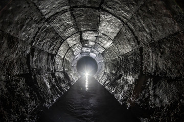 Round drainage concrete tunnel with water built with formwork. With light at the end. Underground...