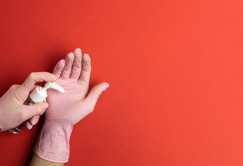 Using hand sanitizer alcohol gel on red background in Medical lab gloves. Clear sanitizer in pump bottle, for killing germs, bacteria. Corona Virus pandemic protection by washing hands frequently