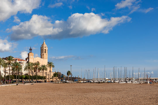Beautiful view of the church Sant Bartomeu and Santa Tecla in Sitges with boats on the beach under the beautiful sky.