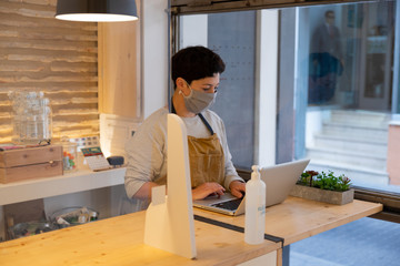 Female caucasian entrepreneur wearing face mask working with her laptop in her store, New normal coronavirus pandemic concept