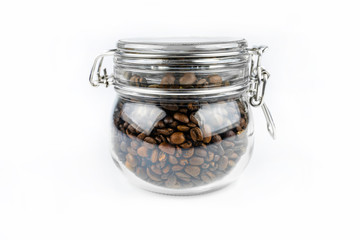 Fresh, roasted coffee beans in a closed transparent jar standing on a white table.