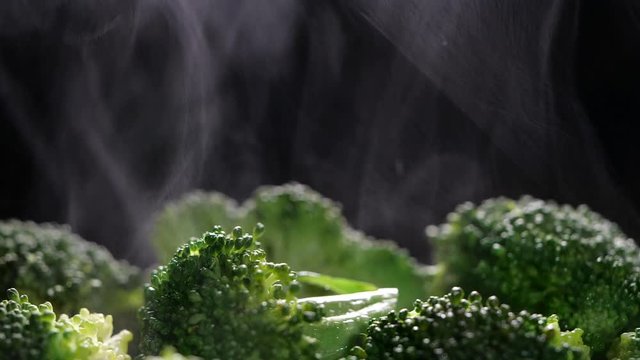 Boiling broccoli with steam in slow motion. Cocking broccoli on black background