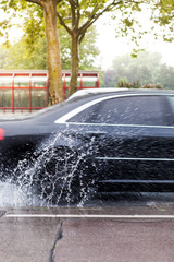 Auto fährt schnell durch Wasserlacke. Auto fährt im Regen. Auto spritzt im Strassenverkehr. Car drives quickly through water-based paints. Car drives in the rain. Car splashes in traffic.