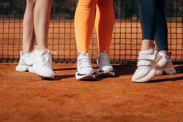 White sneakers on three girls legs on the tennis court background