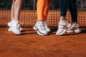 Fototapeta na wymiar White sneakers on three girls legs on the tennis court background