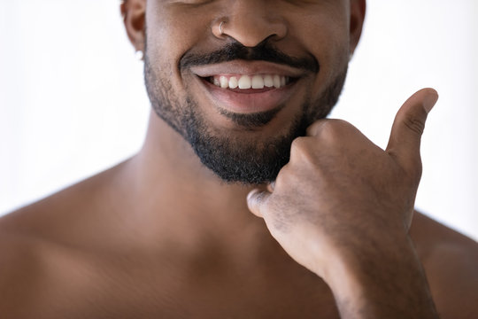 Crop close up of happy african American young man touch beard stubble after shaving in bathroom, smiling biracial male satisfied with shaved bristle after shower in bath, body hygiene concept