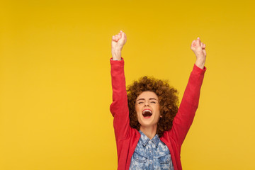 Hurray, I am champion! Portrait of ecstatic happy woman with curly hair shouting joyfully and raising hands, excited about victory, successful achievement. studio shot isolated on yellow background
