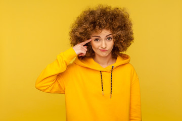 This is crazy! Portrait of curly-haired woman in urban style hoodie making stupid sign with finger...