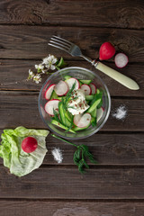 Top view of radish and cucumber salad in a glass bowl on wooden background