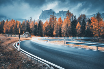 Blurred car on winding road in mountains in overcast rainy evening in autumn. Dramatic landscape...