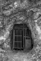 An old mining tunnel sealed off with metal bars. Black and white. Photographed at the abandoned Crown Mine in the Karangahake Gorge, New Zealand
