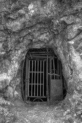 Fototapeta premium An old mining tunnel sealed off with metal bars. Black and white. Photographed at the abandoned Crown Mine in the Karangahake Gorge, New Zealand