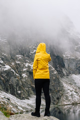 Journey to the mountains. A young woman in a yellow jacket looks at a mountain range covered in snow. A girl stands with her back turned.