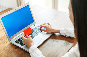 Close-up female hand with a credit card and laptop with blank screen, back view. Online shopping concept, internet banking