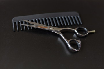 hairdresser tool scissors and comb on a black background, place for an inscription